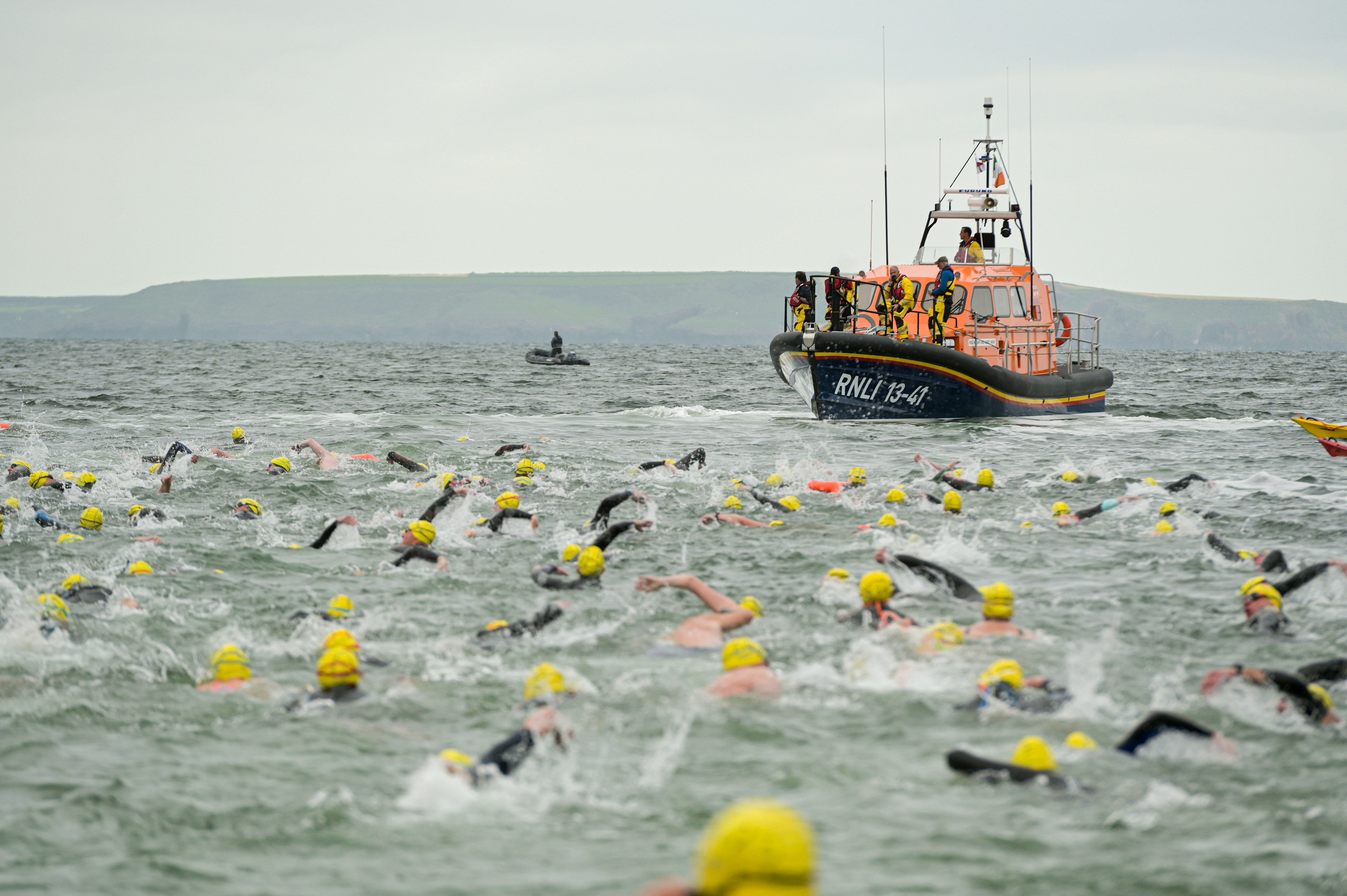 Swimmers take part in an RNLI open water swim, with an RNLI boat in the background