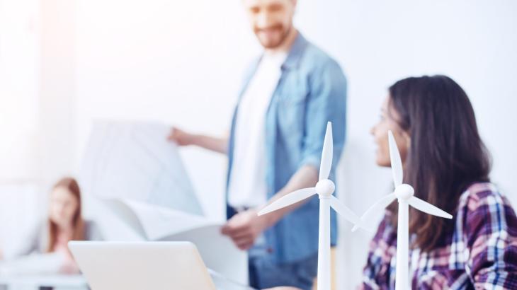 Young professionals discuss a document with models of turbines in the foreground